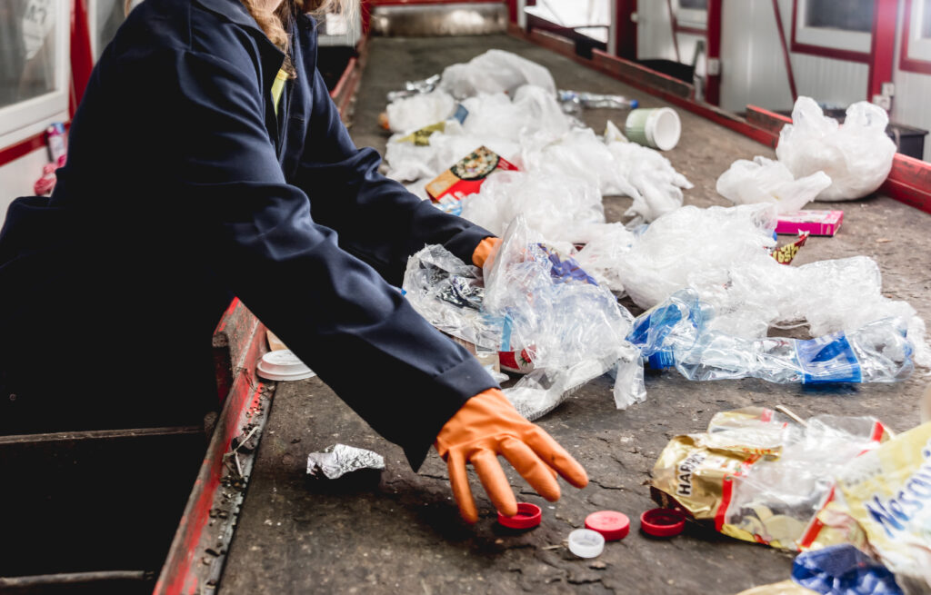 Sur un tapis roulant, on aperçoit un employé doté de gant, en train de trier des déchets plastique.